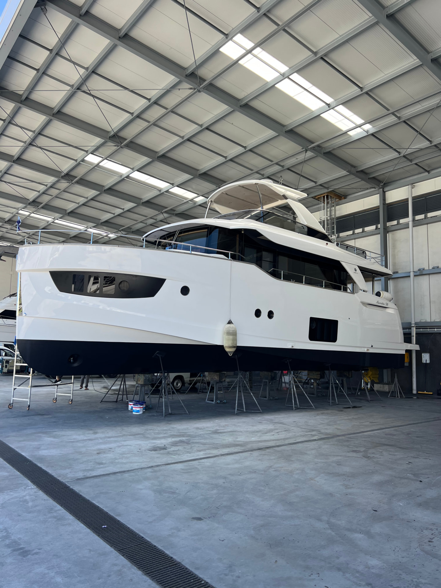 White motor yacht on stands in a shed with freshly applied antifoul