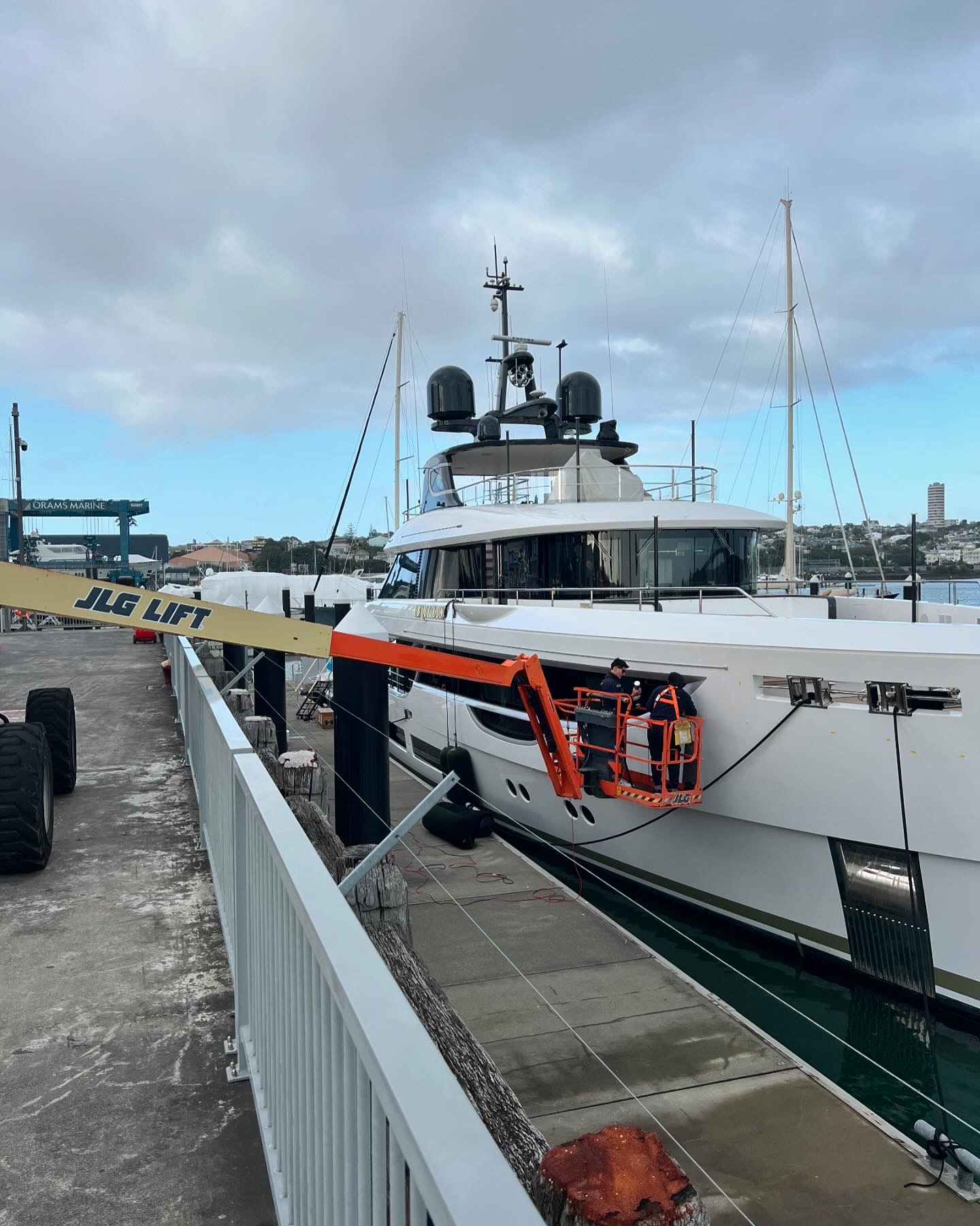 Two technicians on a boom lift detailing the hull of a superyacht at the marina